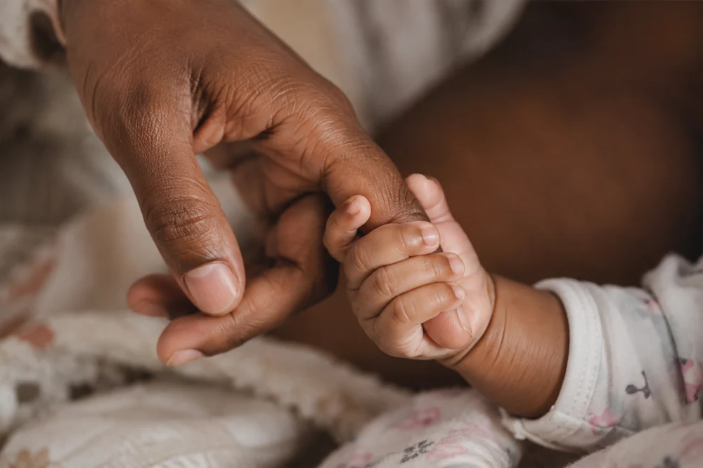 Um bebê envolve com a mão o dedo de uma pessoa adulta.